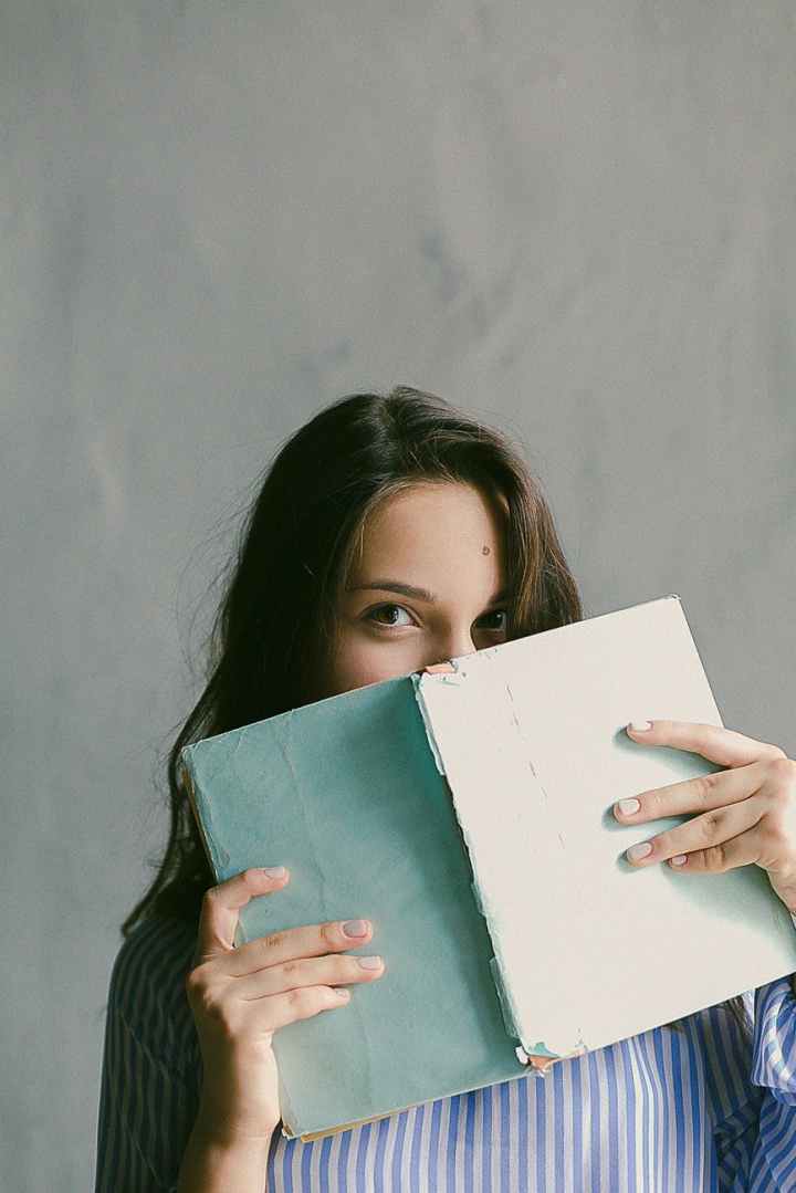 woman in blue striped flannel shirt holding a book indoors