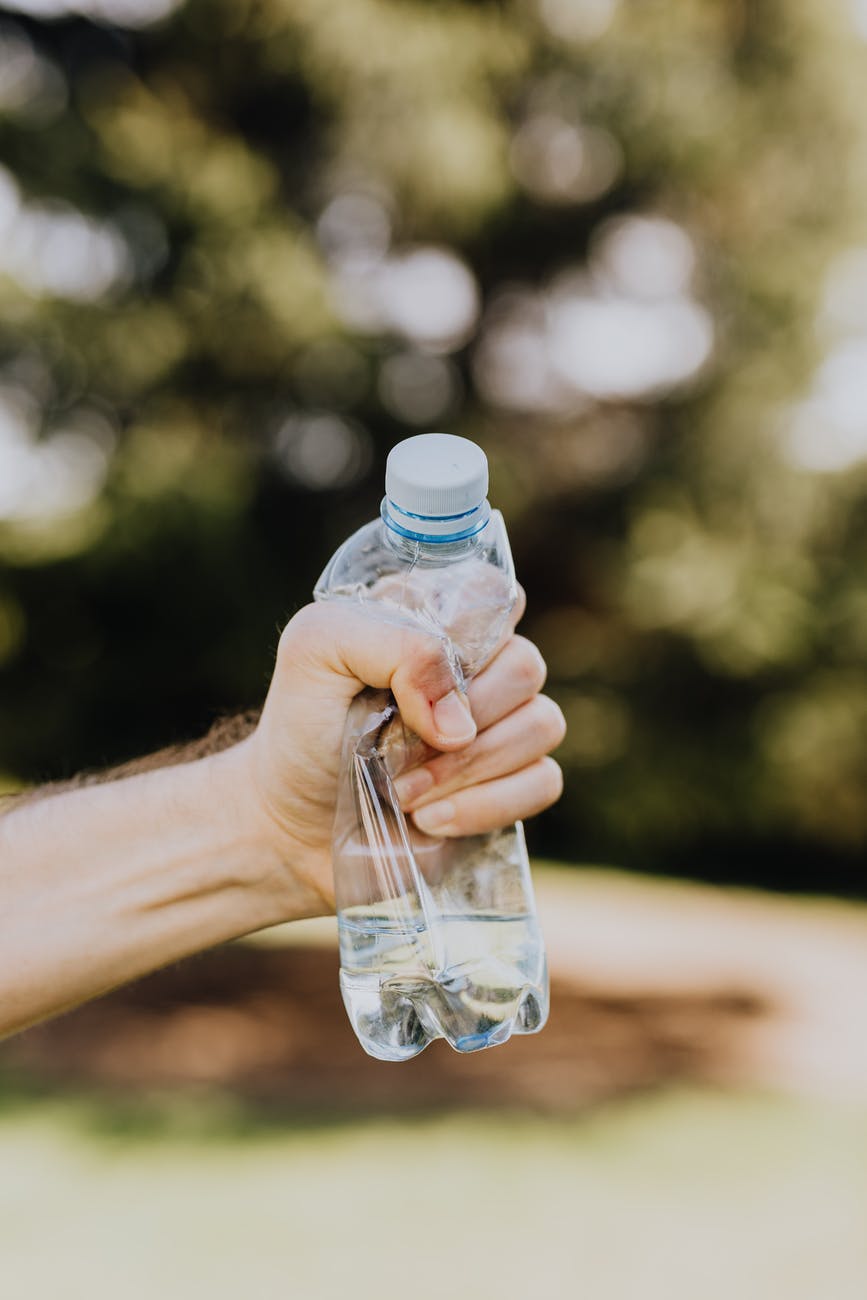 crop male crushing plastic water bottle in park